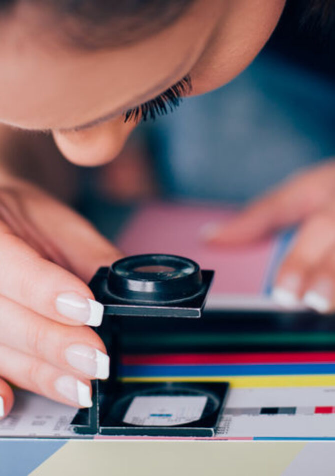 Worker in a printing and press centar uses a magnifying glass and check the print quality